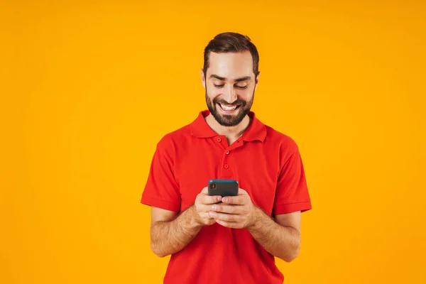 Portrét radostného muže v červeném tričku s úsměvem a přidržením smartp — Stock fotografie