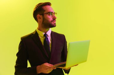 Konsantre genç iş adamı dizüstü bilgisayar kullanarak led neon ışıkları ile açık yeşil arka plan duvar üzerinde izole poz.