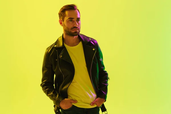 Knappe jonge stijlvolle man poseren geïsoleerd over licht groene achtergrond muur met LED neonlichten gekleed in lederen jas. — Stockfoto