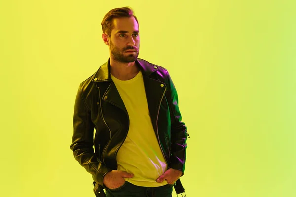 Bonito jovem elegante homem posando isolado sobre a parede de fundo verde claro com luzes de néon led vestida com jaqueta de couro . — Fotografia de Stock