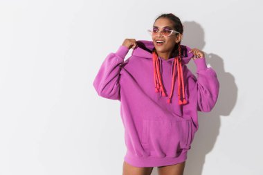 Pembe sweatshirt ve güneş gözlüğü beyaz duvar arka plan üzerinde izole poz Gülümseyen neşeli mutlu afrikalı şık kadın.