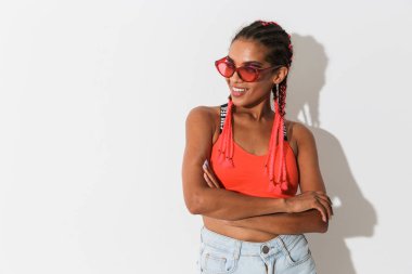 Gülümseyen mutlu genç Afrikalı kadın güneş gözlüğü takarak beyaz duvar arka plan üzerinde izole poz.