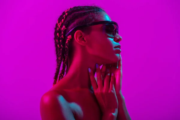 Attractive beautiful young african naked woman posing isolated over purple neon lights wall background wearing sunglasses. — Stock Fotó