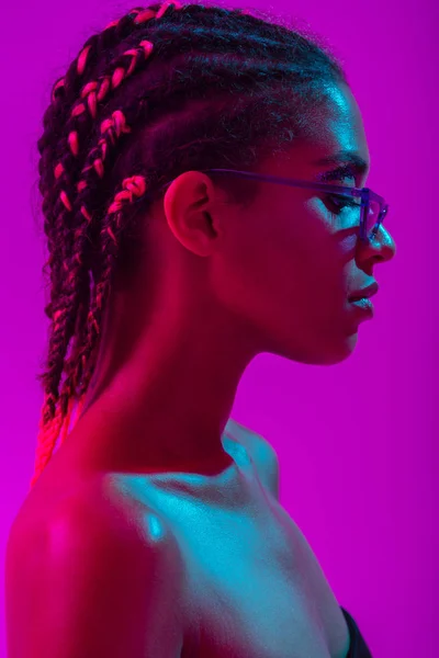 Attraente bella giovane donna africana nuda posa isolata su luci viola al neon sfondo della parete indossando occhiali da sole . — Foto Stock