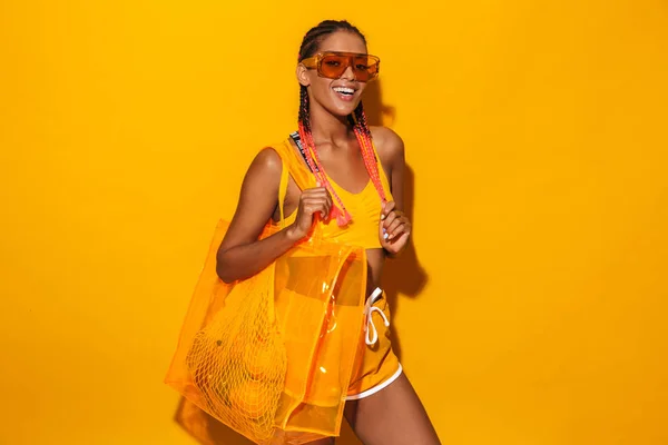 Изображение симпатичной африканской женщины в солнцезащитных очках с пластиковым пакетом и улыбающейся — стоковое фото