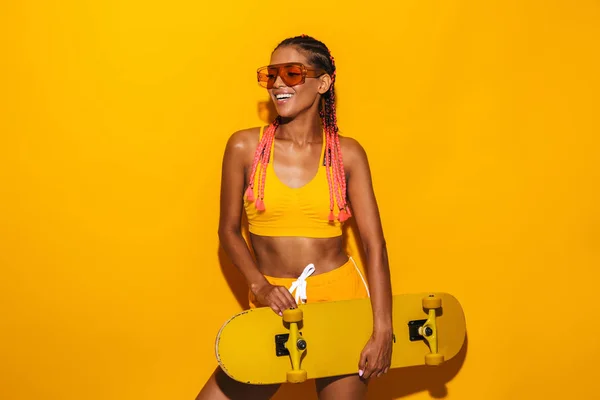 Image of nice african american woman wearing sunglasses holding skateboard and laughing — Stock Photo, Image