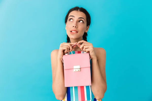 Изображение задумчивой белой женщины с косичками, держащей розовый мешок и кусающей губу — стоковое фото