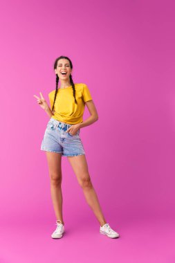 Denim şort giyen genç neşeli kadının tam uzunlukta fotoğraf göz kırpma ve barış işareti gesturing