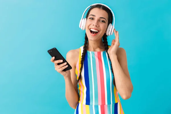 Bild av brunett glad kvinna leende när du använder hörlurar och mobiltelefon — Stockfoto