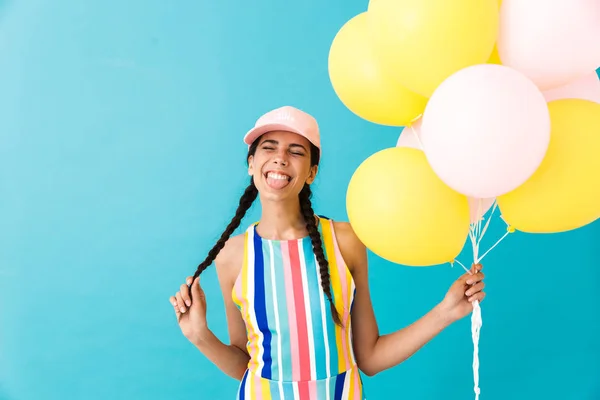 Imagem de mulher alegre bonito usando boné saindo de sua língua enquanto segurando balões de ar — Fotografia de Stock