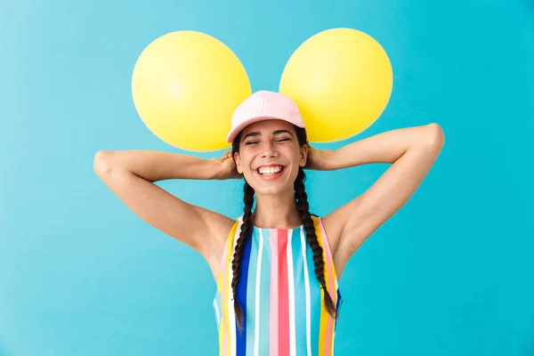 Wizerunek miłej radosnej kobiety noszenie czapki śmiejąc się z zamkniętymi oczami trzymając dwa balony powietrzne — Zdjęcie stockowe