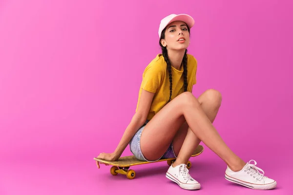 Imagem de mulher caucasiana sedutora vestindo roupas casuais olhando para a câmera e sentado no skate — Fotografia de Stock