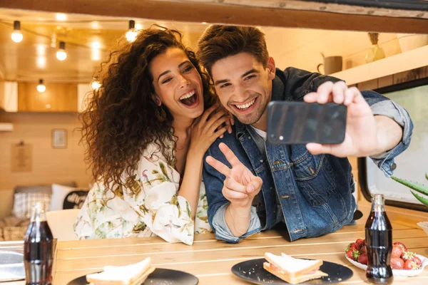 Retrato de casal feliz gesticular sinal de paz ao tirar foto selfie no smartphone na cozinha acolhedora em reboque dentro de casa — Fotografia de Stock