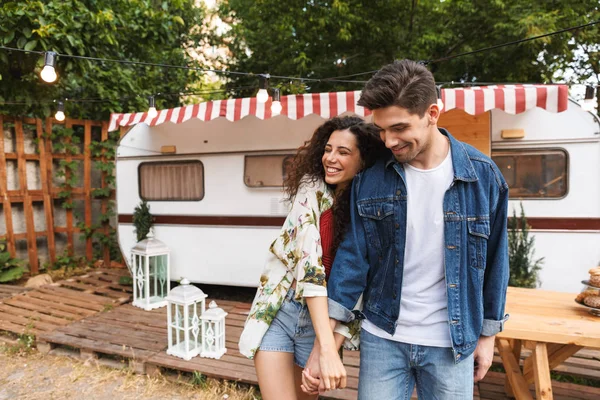 Portret van romantisch paar glimlachend tijdens het vasthouden van de handen in de buurt van huis op wielen buitenshuis — Stockfoto