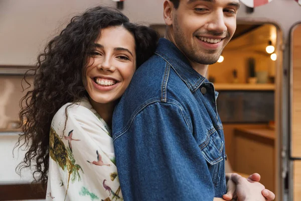 Retrato de casal romântico sorrindo enquanto abraçando juntos perto de casa sobre rodas ao ar livre — Fotografia de Stock