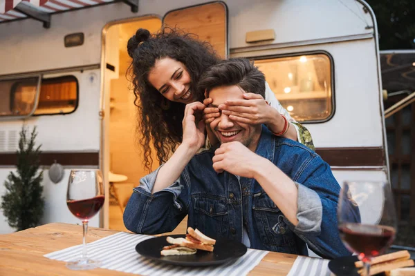 Retrato de una bonita mujer sonriente cubriendo los ojos de su novio en la cena cerca del remolque al aire libre — Foto de Stock