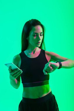 Saat saat bakarak cep telefonu kullanarak neon parlak ışıklar ile mavi duvar arka plan üzerinde izole Spor kadın.