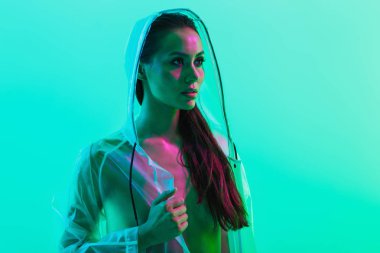 Ciddi kadın yağmurluk giymiş neon parlak ışıklar ile mavi duvar arka plan üzerinde izole poz.