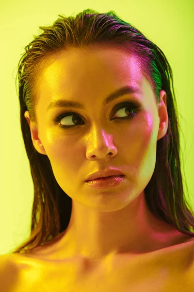 Hermosa joven posando aislada sobre fondo de pared amarillo con luces brillantes de neón . — Foto de Stock