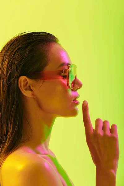 Mulher nova surpreendente posando isolado sobre fundo de parede amarelo com luzes brilhantes de néon vestindo óculos de sol de moda . — Fotografia de Stock