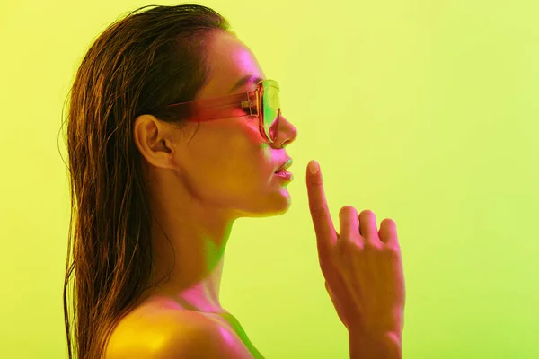 Mulher nova surpreendente posando isolado sobre fundo de parede amarelo com luzes brilhantes de néon vestindo óculos de sol de moda . — Fotografia de Stock