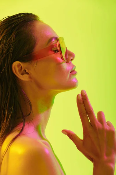 Incroyable jeune femme posant isolé sur fond de mur jaune avec néon lumières lumineuses portant des lunettes de soleil de mode . — Photo