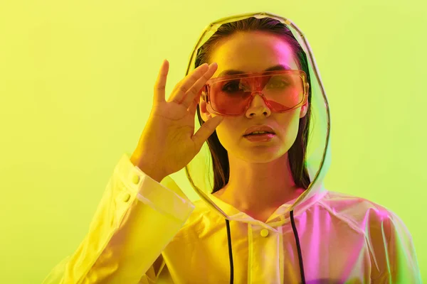 Incroyable jeune femme posant isolé sur fond de mur jaune avec néon lumières lumineuses portant des lunettes de soleil de mode . — Photo