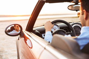 Deniz kenarında üstü açık araba kullanan neşeli yakışıklı adamın fotoğrafı 