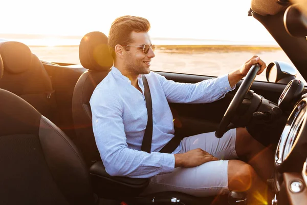 Foto de atractivo hombre caucásico conduciendo un coche descapotable por mar —  Fotos de Stock