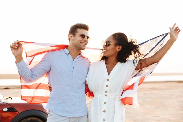 Foto de alegre pareja multiétnica sonriendo y sosteniendo a los americanos — Foto de Stock