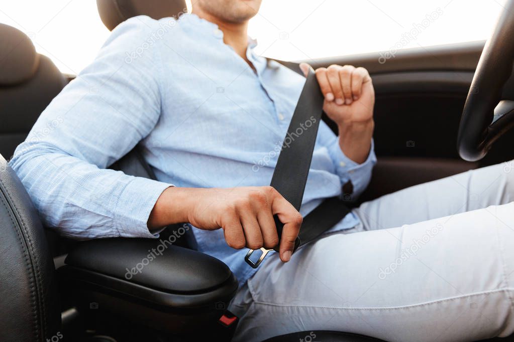 Cropped photo of young man wearing seat belt while driving conve