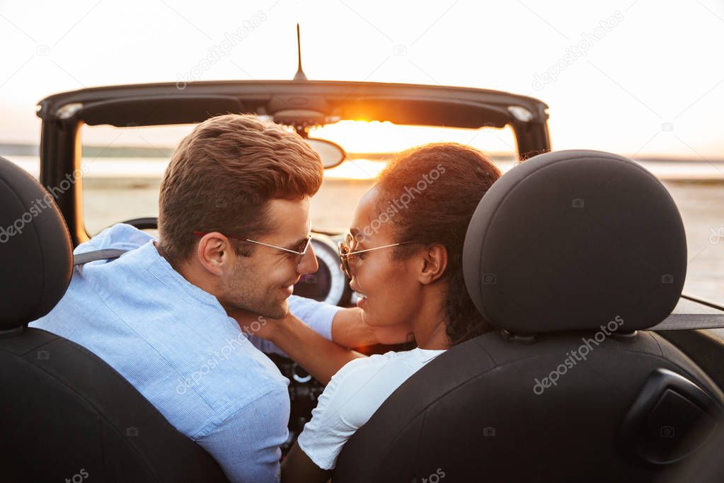 Image of attractive multiethnic couple kissing while siting in c