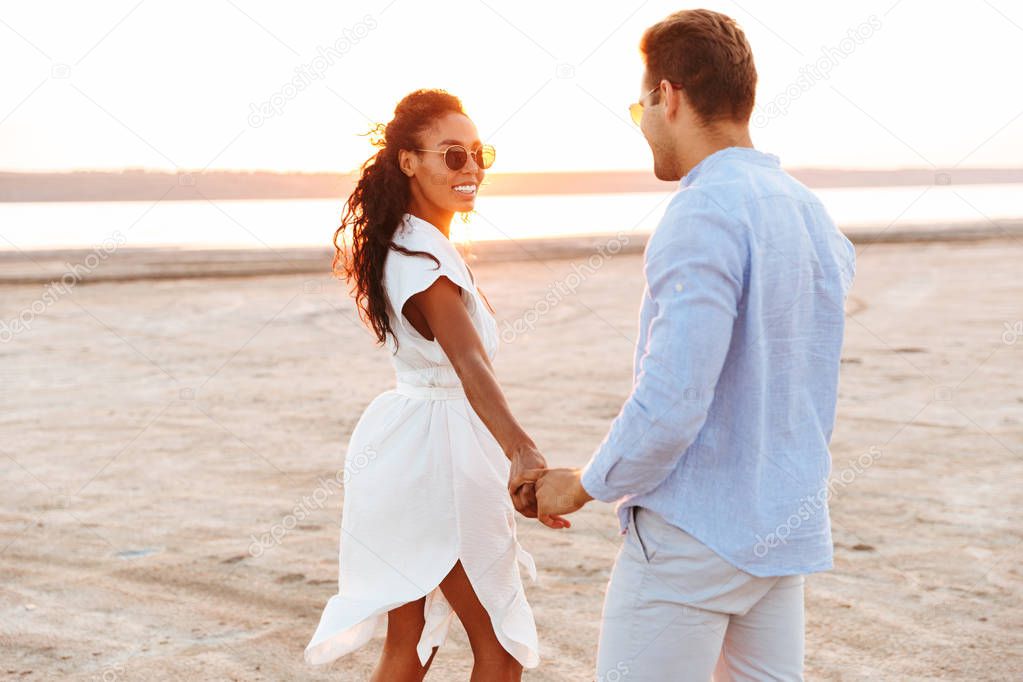 Image of stylish multiethnic couple smiling and holding hands to