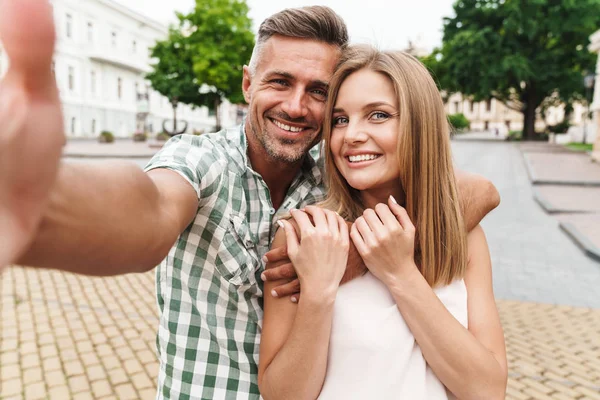 Immagine di affascinante giovane coppia sorridente e scattare foto selfie insieme mentre si cammina per la strada della città — Foto Stock