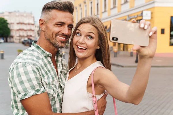 Foto di una giovane coppia amorevole che sorride e si abbraccia insieme mentre scatta foto selfie sulla strada della città — Foto Stock