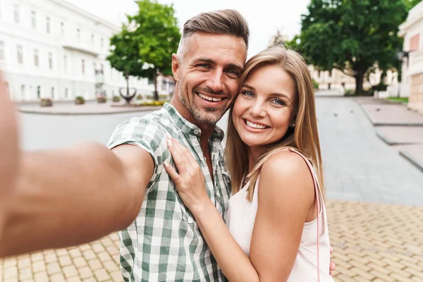 Imagem de belo casal jovem sorrindo e tirando foto selfie juntos enquanto caminhava pela rua da cidade — Fotografia de Stock