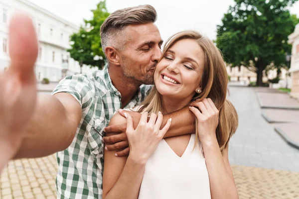 Immagine di amare la giovane coppia baciare e scattare foto selfie insieme mentre si cammina per la strada della città — Foto Stock
