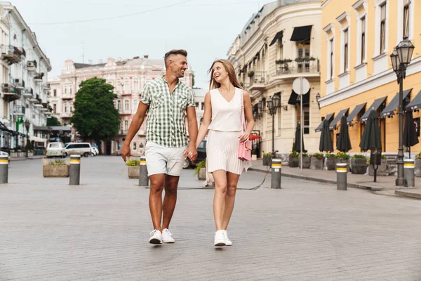 Imagem de casal feliz caucasiano sorrindo e de mãos dadas enquanto caminhava pela rua da cidade — Fotografia de Stock