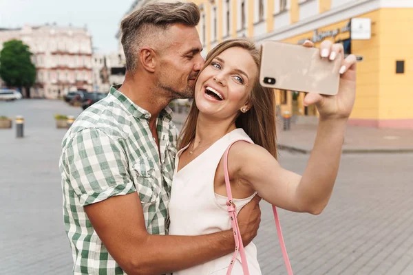 Foto von entzückenden jungen Paar lächelt und umarmt zusammen, während Selfie-Foto auf der Straße der Stadt — Stockfoto