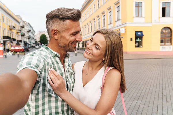 Foto di attraente coppia amorevole sorridente e abbracciarsi insieme mentre scattano foto selfie sulla strada della città — Foto Stock