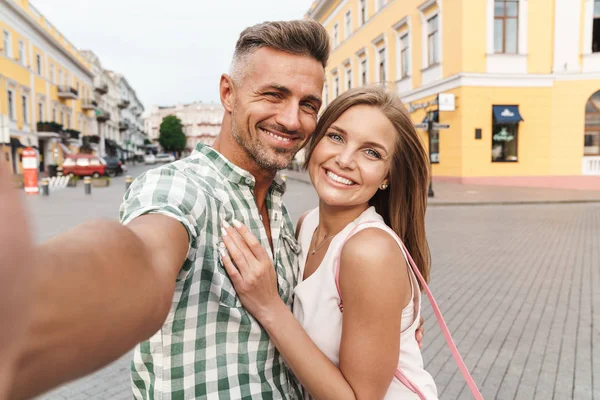Foto della giovane coppia bionda che sorride e si abbraccia insieme mentre scatta foto di selfie sulla strada della città — Foto Stock