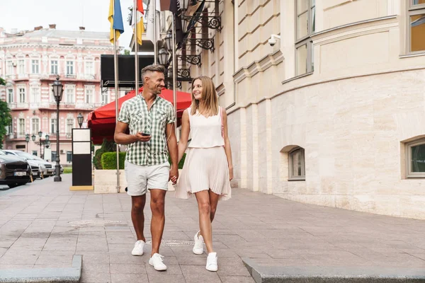 Imagem de belo jovem casal ouvindo música junto com fones de ouvido enquanto caminhava pela rua da cidade — Fotografia de Stock