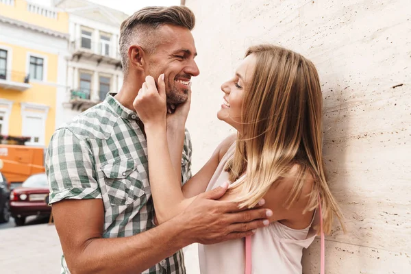 街の通りで壁に立ちながら、一緒に微笑んでいちゃつく魅力的なブロンドカップルのイメージ — ストック写真