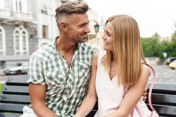 Porträt eines zufriedenen jungen Paares, das auf einer Bank in der Stadtstraße lächelt und sich umarmt — Stockfoto