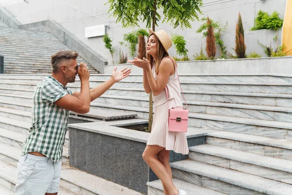 Immagine di uomo felice fotografare giovane bella donna sulla macchina fotografica retrò alle scale della città — Foto Stock