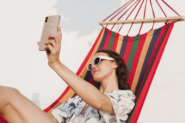 Jovem mulher bonita na praia posando em uma rede tirar uma selfie por telefone celular . — Fotografia de Stock