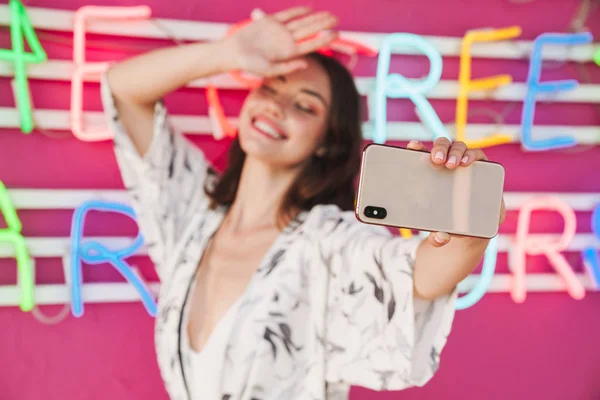 Радостная молодая красивая женщина на пляжной вечеринке с ярким цветным фоном с весельем сделать селфи по мобильному телефону . — стоковое фото