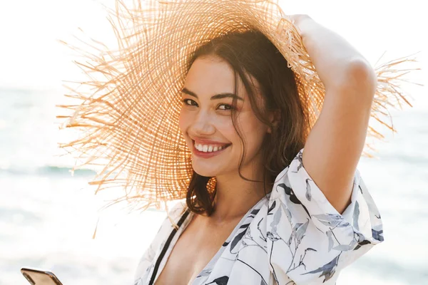 Lächeln erfreut glücklich junge schöne Frau am Strand zu Fuß in einem schönen sonnigen Morgen mit Mobiltelefon. — Stockfoto