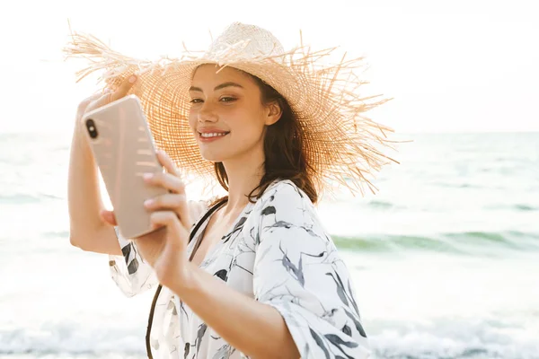 Ευτυχής χαρούμενη νεαρή όμορφη γυναίκα στην παραλία με τα πόδια σε ένα όμορφο ηλιόλουστο πρωί να πάρει μια selfie από το κινητό τηλέφωνο. — Φωτογραφία Αρχείου