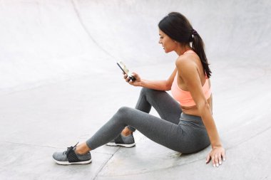 Boks eldivenleri ile beton zeminde otururken cep telefonu tutan atletik genç kadın Görüntü